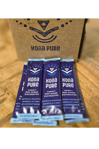 Kona Pure electrolyte packets on a wooden surface with a cardboard box in the background.